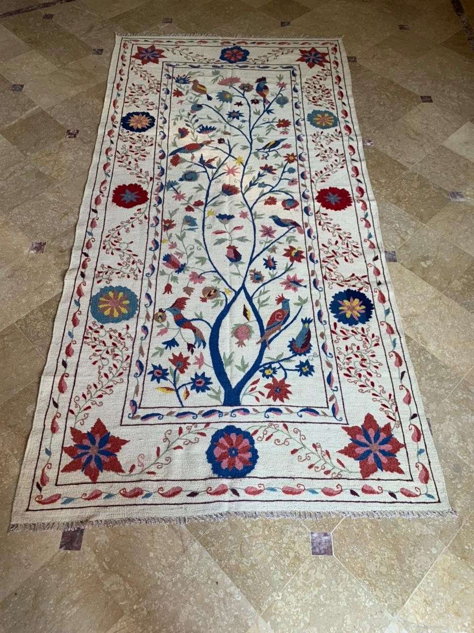 Decorative rug with floral and bird pattern on a beige tiled floor