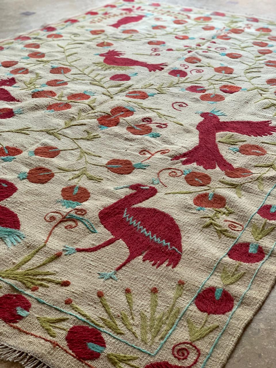 Close-up of a decorative rug with red bird and floral patterns on a beige background