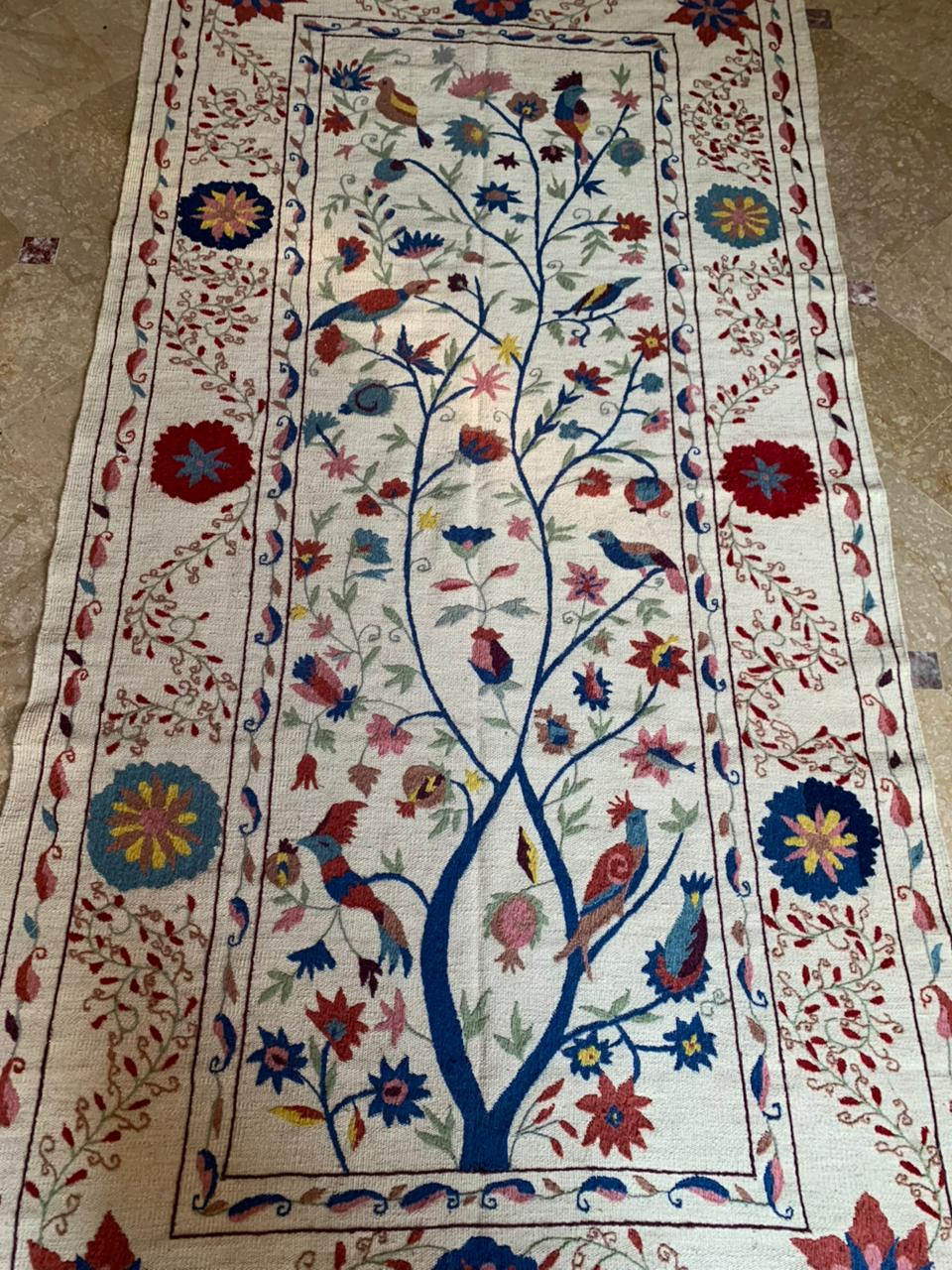 Decorative rug with floral and bird patterns on a beige floor.
