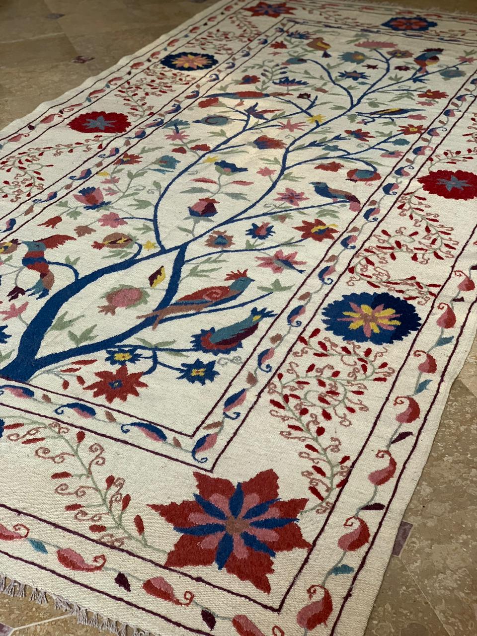 Decorative rug with floral and bird patterns on a beige floor.